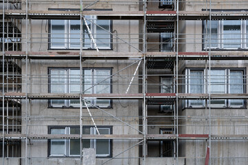 Fototapeta na wymiar Facade wall on a construction site in Europe, Scaffolding among windows. Unfinished modern apartment architecture building site.
