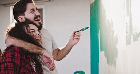 Young Caucasian happy just-married wife and husband moving in their new home and before that painting walls in blue colour as doing repair and renovation.
