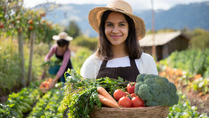 Portrait of smiling female gardener holding basket with harvested vegetables on farm