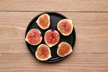 Plate with halves of fresh ripe figs on wooden background