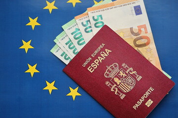 Red Spanish passport of European Union and money on blue flag background close up. Tourism and...