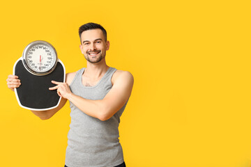 Handsome sporty young man with scales on yellow background. Weight loss concept