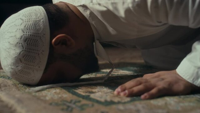 Ground level side footage of unidentified bearded muslim man bowing taking sajdah position with head on prayer mat while performing salat and expressing gratitude to Allah