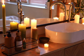 Cosmetic products with burning candles and sink in bathroom at night, closeup