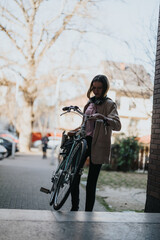 A stylish young woman engages with her smart phone beside her parked bicycle on a sunny city street.