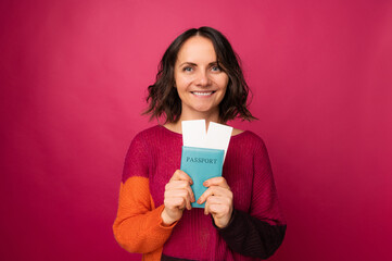 Studio portrait of a beautiful smiling middle age woman holding her passport with two flight tickets.