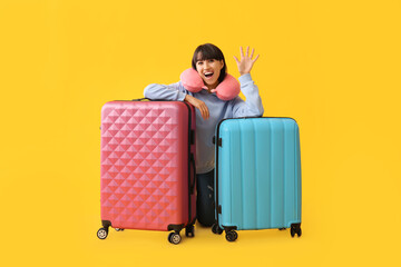Female tourist with suitcases waving hand on yellow background