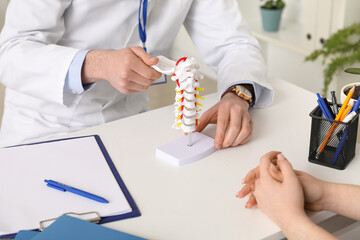 Male doctor explaining spinal anatomy with vertebral column model to patient in clinic, closeup