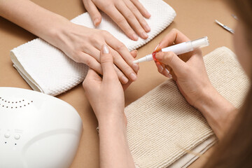 Manicure master applying cuticle oil onto female fingernails on brown background