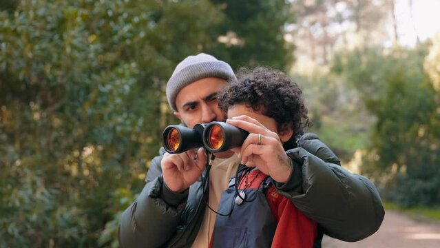 A father and his young son using binoculars together during a nature walk in the forest, exploring and bonding.