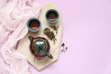 Marble tray with teapot, cups of tea and dry pressed tea on purple background