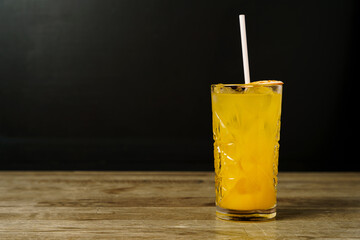 A cocktail with a slice of dried orange and ice on a wooden table