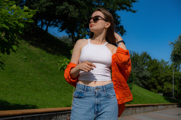 A beautiful smiling girl fixes her hair in a green park in a modern city