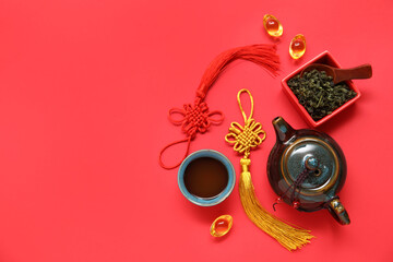 Composition with teapot, cup of tea and bowl with dry leaves on red background