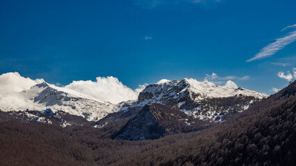 The snow-capped mountains of the Abruzzo Apennines, in Campo Felice, Italy. Below, a beech forest, with bare trees in winter. The white clouds on the rocky mountain peaks.