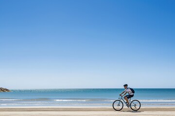 A man riding a bike along the sandy beach next to the ocean on a sunny day.