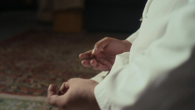 Side closeup of anonymous muslim person counting number of said prayers using phalanges on left hand indoors