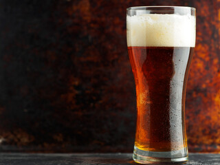 glass of amber lager beer on an iron background, copy space - obrazy, fototapety, plakaty