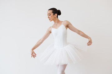 Fototapeta na wymiar Caucasian ballerina in white bodysuit and tutu poses in motion showing ballet elements while standing on pointe shoes. Beautiful young female dancer posing on studio background.