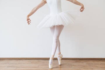 Close up of legs of Caucasian ballerina in white bodysuit and tutu poses in motion showing ballet elements while standing on pointe shoes.