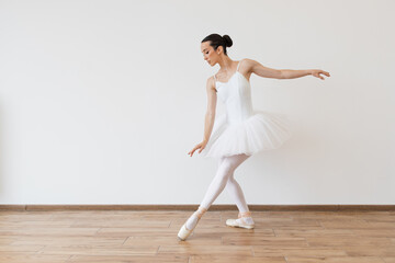 Caucasian ballerina in white bodysuit and tutu poses in motion showing ballet elements while...