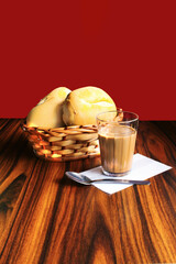 Breakfast in Brazil with coffee and milk glass and basket with brazilian breads in a red background.