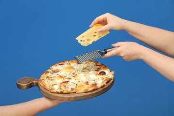 Woman adding cheese to tasty pizza on blue background