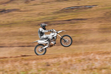 Obraz premium A man on a motocross bike performs an offroad trick with his helmet on