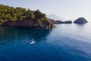 Fototapeta na wymiar Aerial view of young woman in bikini using long paddle for floating on sup board in Mediterranean sea