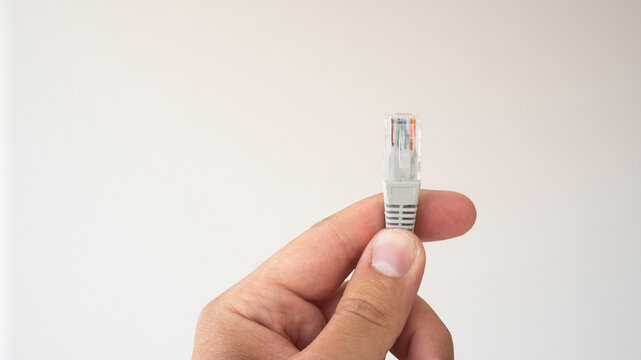 LAN ethernet cable in hand. Gray RJ45 twisted pair cable for computer network. Cat 5e UTP connection. White isolated background.