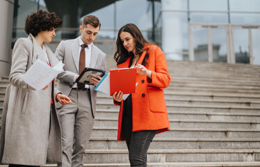 Obraz premium Three business colleagues engaging in a discussion with documents and digital tablet on the steps outside their office building.