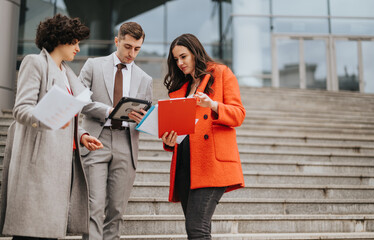 Three business colleagues engaging in a discussion with documents and digital tablet on the steps outside their office building.