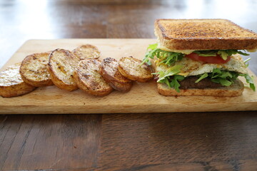 delicious toasted club saandwich with vegetables dressing and baked potatoes on a wooden board