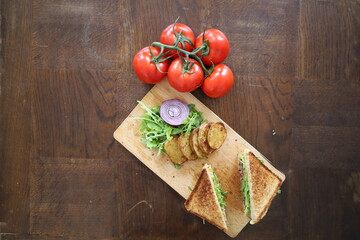 topview flatlay of delicious toasted club saandwich with vegetables dressing and baked potatoes on a wooden board