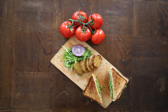 topview flatlay of delicious toasted club saandwich with vegetables dressing and baked potatoes on a wooden board