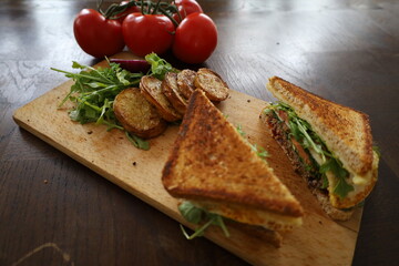 delicious toasted club saandwich with vegetables dressing and baked potatoes on a wooden board