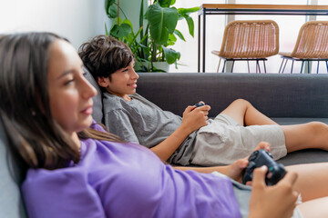 Close-up of two teenagers playing with a video game console lying on a sofa.