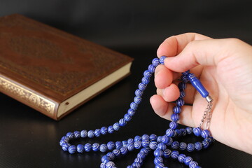 hand of muslim praying with rosary on quran background