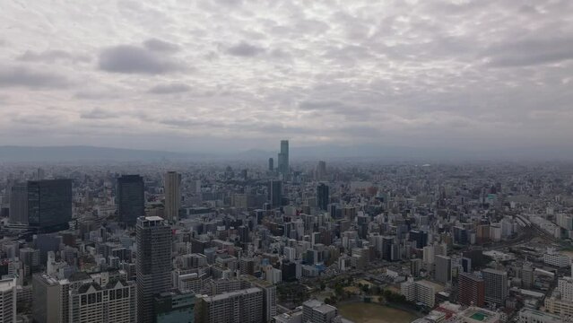 Aerial ascending view of cityscape with modern high rise buildings. Cloudy sky above large city. Osaka, Japan