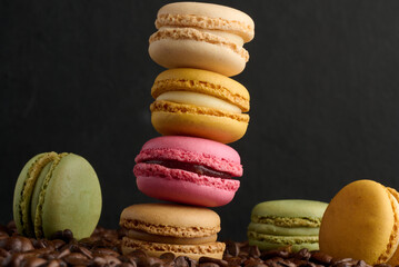 Stack of multi-colored macarons on a background of coffee beans, black background