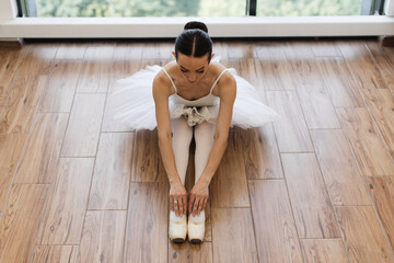 Classical Ballet dancer. Beautiful Caucasian graceful female ballerina in tutu skirt sitting at...