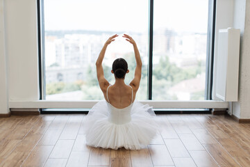 Focused young ballerina dressed in white tutu costume practice ballet poses at ballet studio. Back...