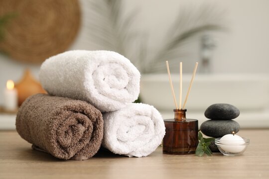 Spa composition. Rolled towels, aroma diffuser, massage stones and burning candle on wooden table indoors