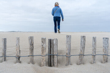 une barrière en bois ensevelie dans le sable avec une femme de dos en fond - 750965758