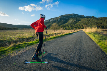 un skieur de dos sur des ski-roues sur une route goudronnée à la campagne
