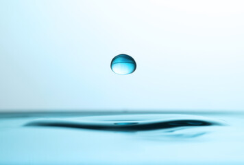 Drop falling into clear water on light background, closeup