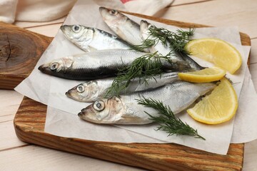 Fresh raw sprats, lemon and dill on light wooden table, closeup