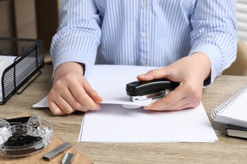 Woman with papers using stapler at wooden table indoors, closeup