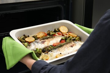 Woman taking baking dish with delicious fish and vegetables from oven, closeup