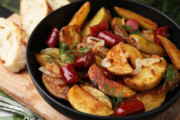 Delicious baked potato with thin dry smoked sausages, onion and dill in bowl on table, closeup